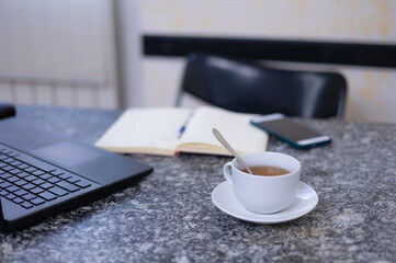 Business man desktop. On the black marble table are a laptop, a cell phone, a notepad, a cup of tea. International Tea Day