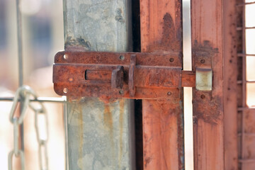 Rusty metal padlock locked on steel rod forbid, even it is old, the entrance in the building. Weathered vintage damaged closed exterior door