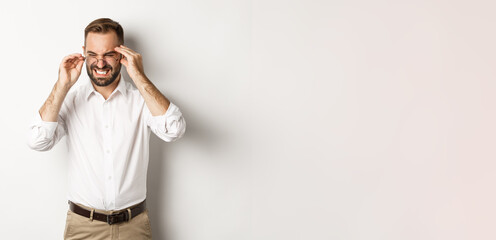 Businessman having headache, grimacing and holding hands on head, standing over white background