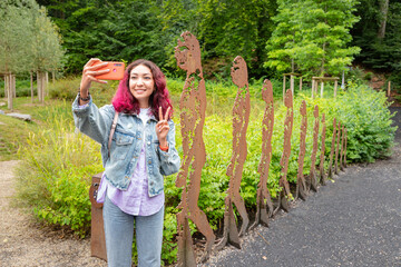 Funny modern girl taking selfie photo in a row of prehistoric ancestors on a children playground...