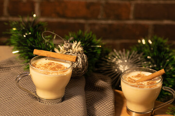 two eggnog cups, green garland with two silver balls, table in two heights with a light grey clown and red brick background with space for text.