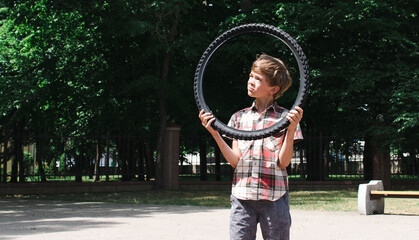A little boy walks in the park, carries a tire from a bicycle