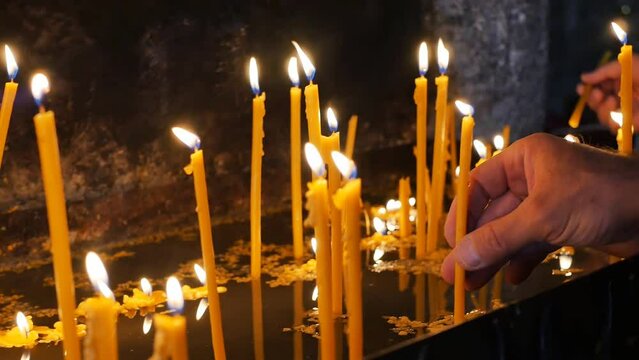 Human hands light candles in the temple on the altar and insert them while standing. The concept of faith in god and asking for help from the Almighty with the help of prayer in the temple