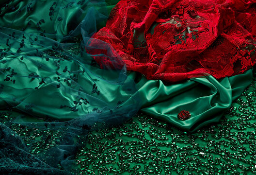 Top view on a natural luxury green silk fabric with rhinestones embroidery and red luxurious lacey fine fabric