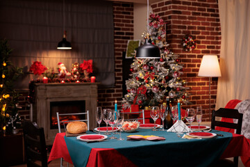 Christmas served dining table, family festive dinner preparation, beautiful decorated place. Wine glasses, dish plates, candles, tableware on traditional red and green tablecloth