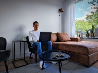 White man in casual clothes works from home with a laptop on his lap in the living room to work on his business and make it succesful. There are no trademarks in the shot.