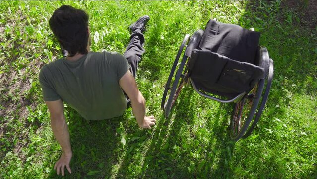 The physically disabled young man lies on the grass and leans against his wheelchair.
Disabled young man lovingly looking at his wheelchair.
