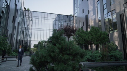 Confident businessman walking office building. Landscaped garden at downtown