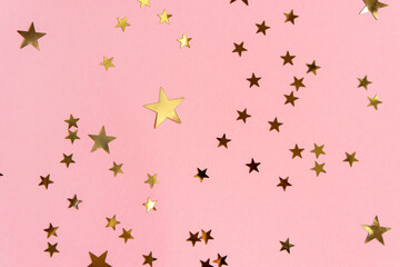 Golden stars glittering confetti on pink background. Trendy festive holiday backdrop. Many star-shaped particles for a postcard, invintation or web banner. 2023 Merry Xmas concept. New Year pattern