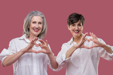 Women in white shirts smiling and showing love sign