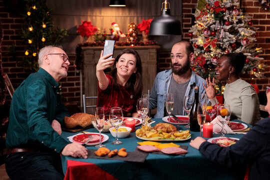 Woman taking family portrait selfie on smartphone, celebrating christmas together at festive dinner table. Xmas holidays celebration, people gathering, eating traditional meal - Powered by Adobe