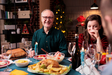 Happy woman celebrating christmas with family, laughing at festive dinner table with dad at home party. Father and daughter eating xmas dishes together, smiling, having fun, looking at camera