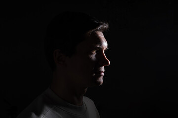 Obraz premium profile of thoughtful man looks to the right. portrait in side light, hard light, photo on black