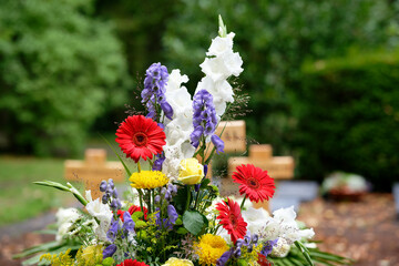 colorful flowers as grave arrangement after a funeral in front of wooden crosses in blurred background