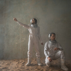 a man and a woman in white futuristic spacesuits explore the planet, astronauts in an empty colony on the sand, A young woman points with her hand somewhere in the distance - 532302367