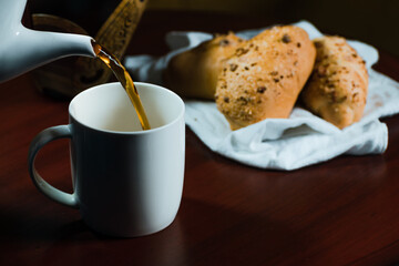 coffee falling into a white porcelain cup with bread next to it on a white handkerchief
