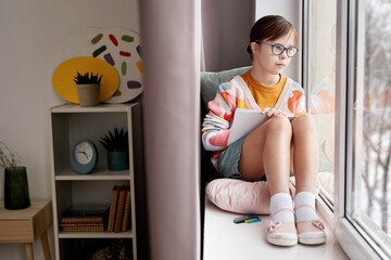 Full length portrait of teenage girl with Down syndrome drawing pictures while sitting by window in...