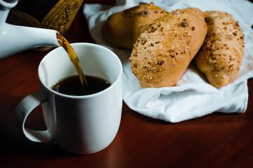 coffee falling into a white porcelain cup with bread next to it on a white handkerchief