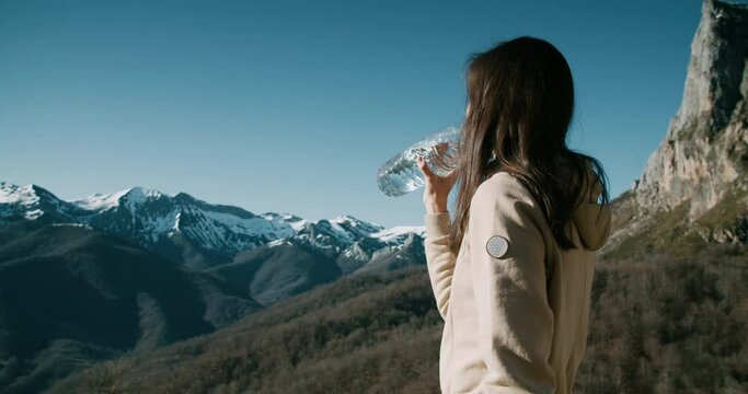 Female traveler on winter vacation trip drink water from bottle on mountain top. Woman enjoying journey adventure taking a break and drinking pure clean water hydrates her body