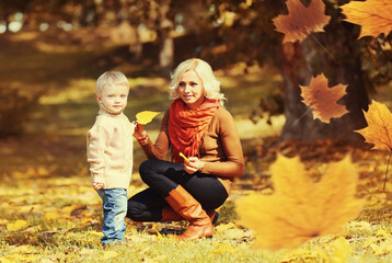 Happy family mother playing with child son in autumn park with yellow leaves