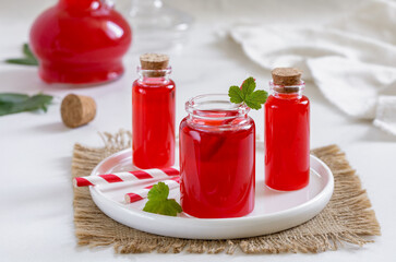 Homemade red berry juice, shrub or syrup in small glass bottles with paper straws on white background - obrazy, fototapety, plakaty