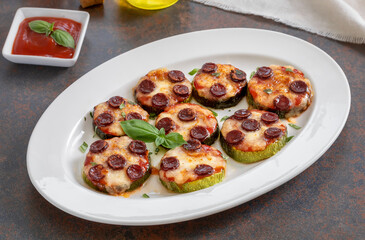 Mini zucchini pizza bites. Grilled zucchini slices with sausage and melted mozzarella cheese served on a white plate with tomato sauce and fresh basil leaves