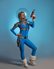 Fantastic astronaut costume in retrofuturism style. A young beautiful blonde in a blue suit with a spherical and helmet with a blaster in a hand. pioneer of space exploration, atomic era, retro style - 532305736