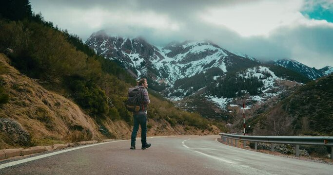 Man on hike trip walk with backpack on empty mountain road photographing epic landscape. Tourist hiking on winter vacation journey. Male photographer surrounded of beautiful nature creating content