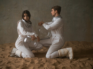 Astronauts on a deserted planet, a man and a woman in white spacesuits with large glass helmets sit...