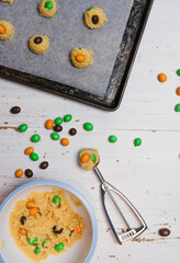 Sugar cookie dough with chocolate candies in Halloween treats colors orange and green, fun baking recipe for kids, scooping raw cookie balls with scoop on baking sheet on white wooden background - 532309534