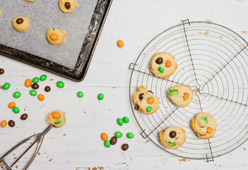 Sugar cookie dough with chocolate candies in Halloween treats colors orange and green, fun baking recipe for kids, scooping raw cookie balls with scoop on baking sheet on white wooden background - 532309580