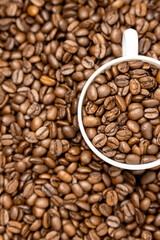 Vertical photo of a cup of coffee full of coffee beans. Top view of white cup and roasted coffee beans.