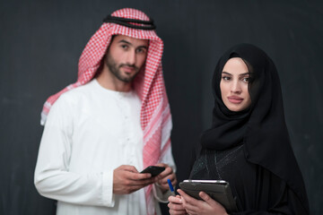 Young muslim business couple in fashionable hijab dress using smartphone and tablet in front of black background