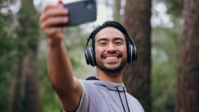 Fitness man, selfie and headphones during forest workout listening to music and taking pictures for social media of influencer content. Happy asian male out for a run, training and exercise in nature