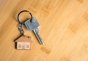 House shaped keychain and key on wood table. Copy space.