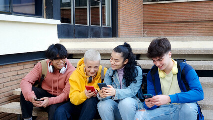 Group of young students sitting on stairs laughing while browsing online on smart phone. Friends have fun 