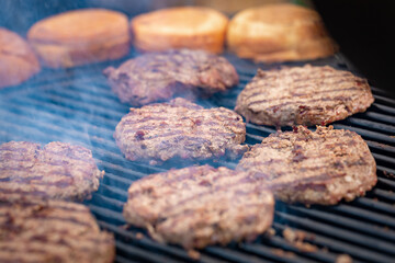 Grilled pork cutlets. Steel grill grate, cutlets in smoke. Pork cutlets for burgers. Fast food or street food. Selected focus, close-up