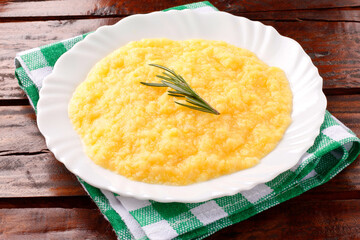 Polenta in white dish on rustic wooden table. Cream of corn or mamaliga