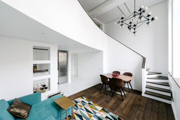 Living room with a green couch, round staircase, modernist chandelier 