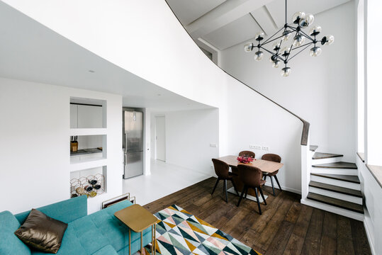 Living room with a green couch, round staircase, modernist chandelier 