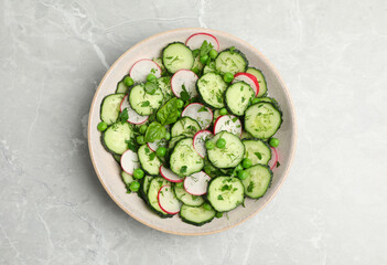 Appetizing salad with cucumbers, radish and pea in bowl on light grey table, top view