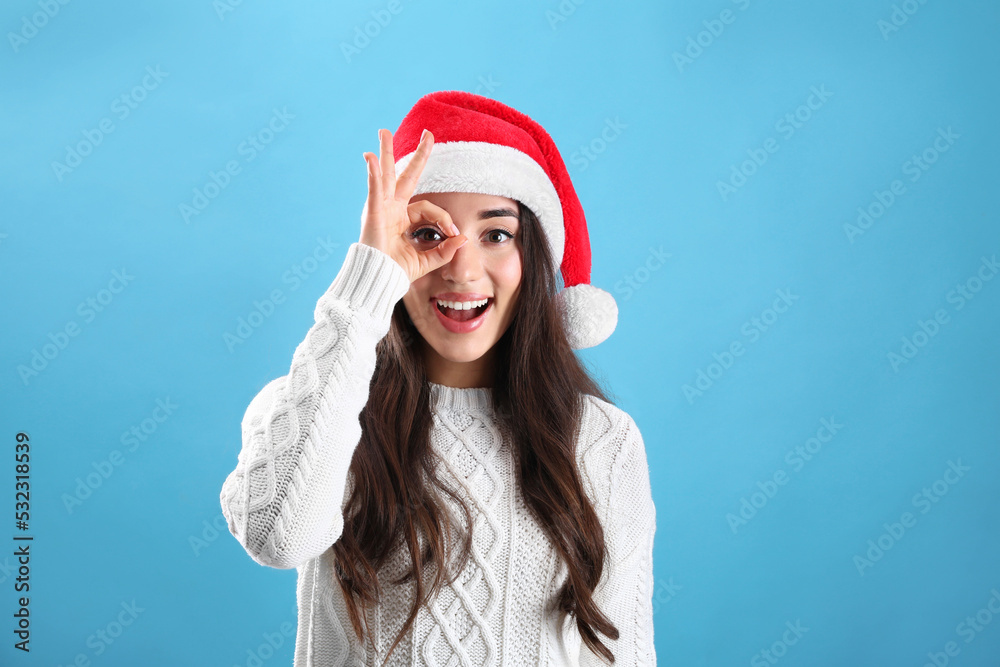 Wall mural beautiful woman wearing santa claus hat on light blue background