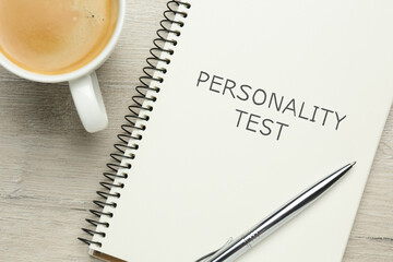 Notebook with text Personality Test, cup of coffee and pen on white wooden table, flat lay