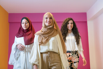 Group portrait of beautiful Muslim women two of them in a fashionable dress with hijab isolated on a pink background