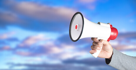 Hand holding a loudspeaker against the sky