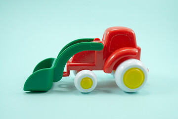 red paint plastic toy bulldozer with green universal blade isolated on turquoise