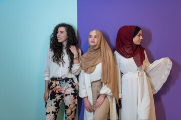 Group portrait of beautiful Muslim women two of them in a fashionable dress with hijab isolated on a colorful background