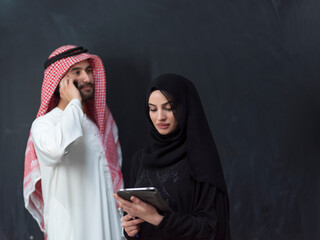 Young muslim business couple in fashionable hijab dress using smartphone and tablet in front of black background