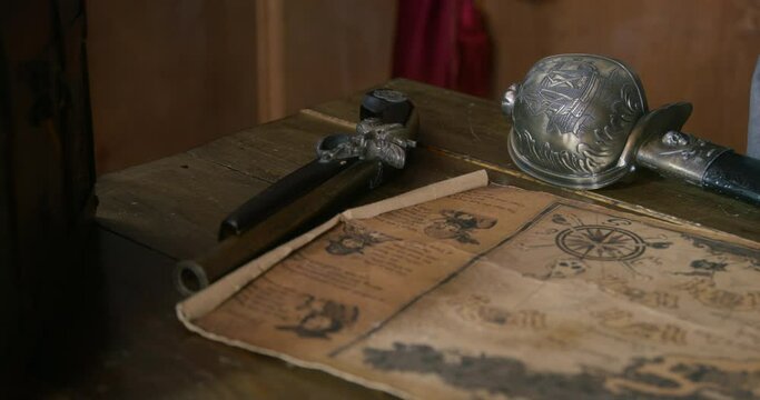 Old table of cabin on which lies ancient treasure map blade and sword, hand of pirate appears. Quest treasure hunt board intellectual game riddle. Animated sea show for children. 