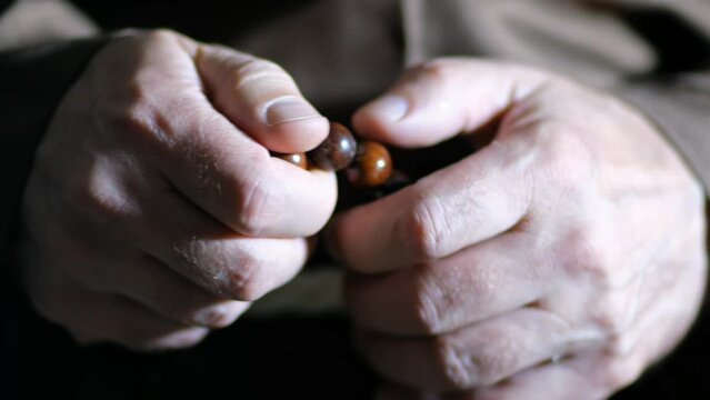Close up video of the hands of a old monk are fingering the rosary.